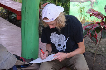 Student writing on a sheet of paper while sitting outside.