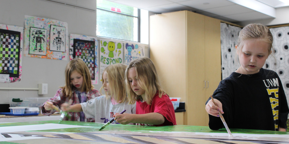 Elementary girls painting artwork on table