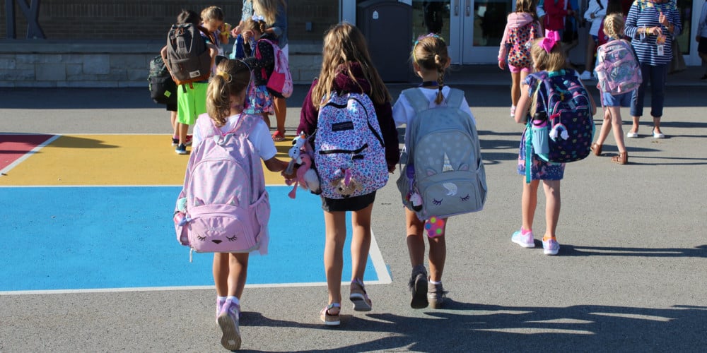 Trio of elementary girls walking into schools with backpacks