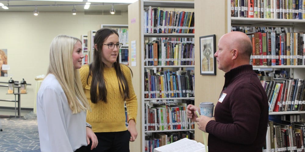 Two girls talking with teacher in library