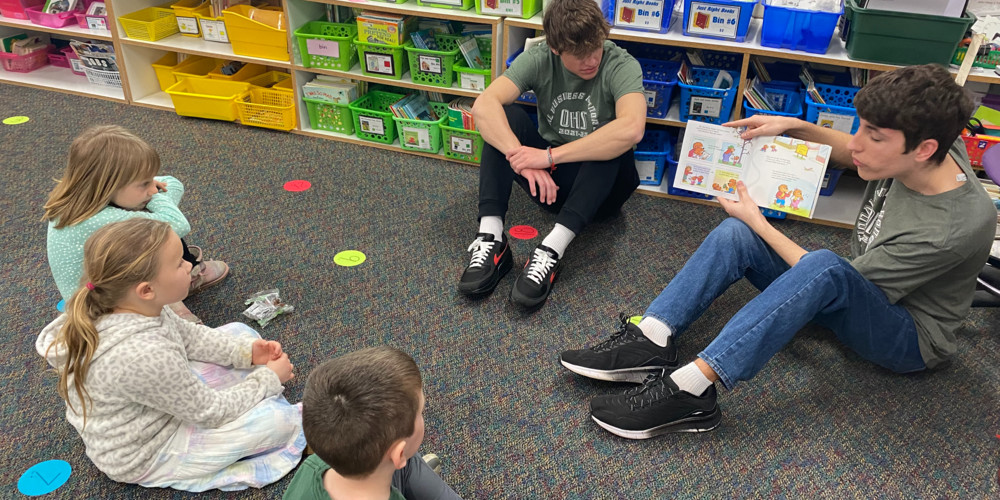 Older student reading to elementary children