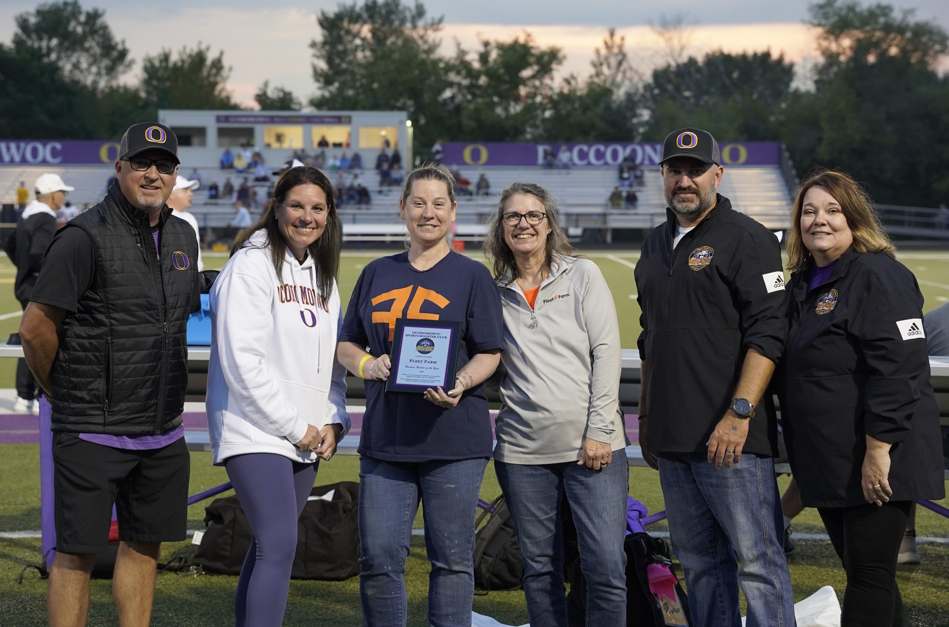 Group photo of six people posing on the sideline of the football field